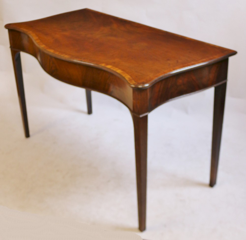 A George III mahogany serving table with a wavy serpentine front, flame mahogany veneer, and four tapered square legs. View IV