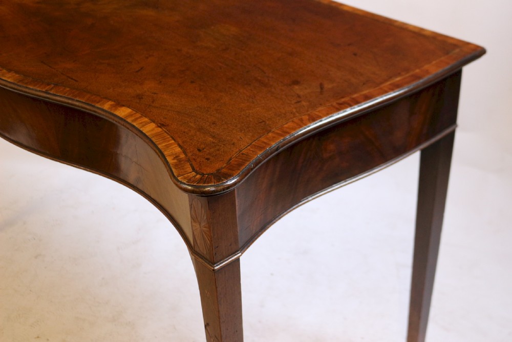 A George III mahogany serving table with a wavy serpentine front, flame mahogany veneer, and four tapered square legs. View V