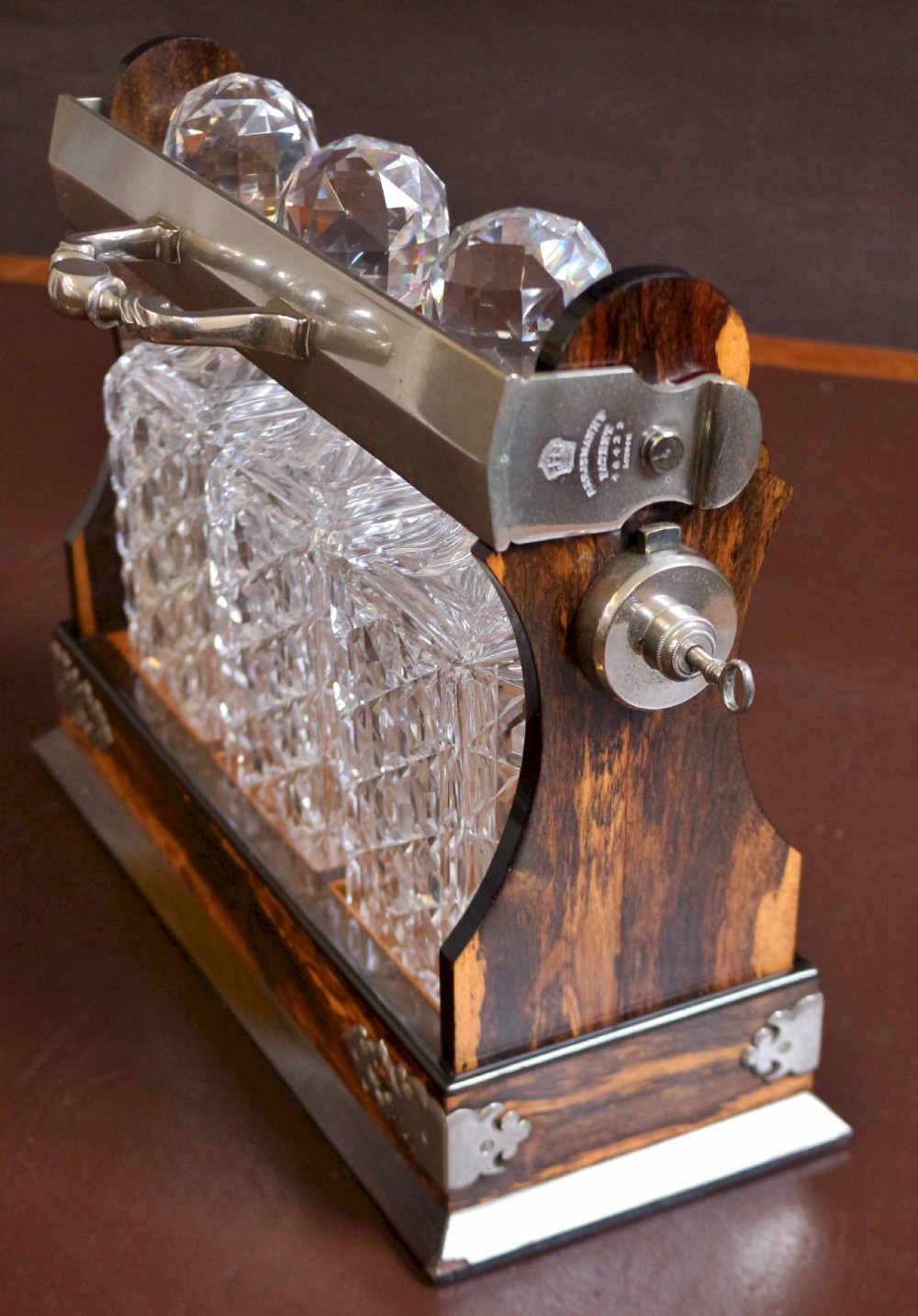 A late Victorian three-bottle tantalus constructed from dark figured coromandel wood with silver-plated corner mounts and three square cut-crystal decanters with faceted stoppers. View IV