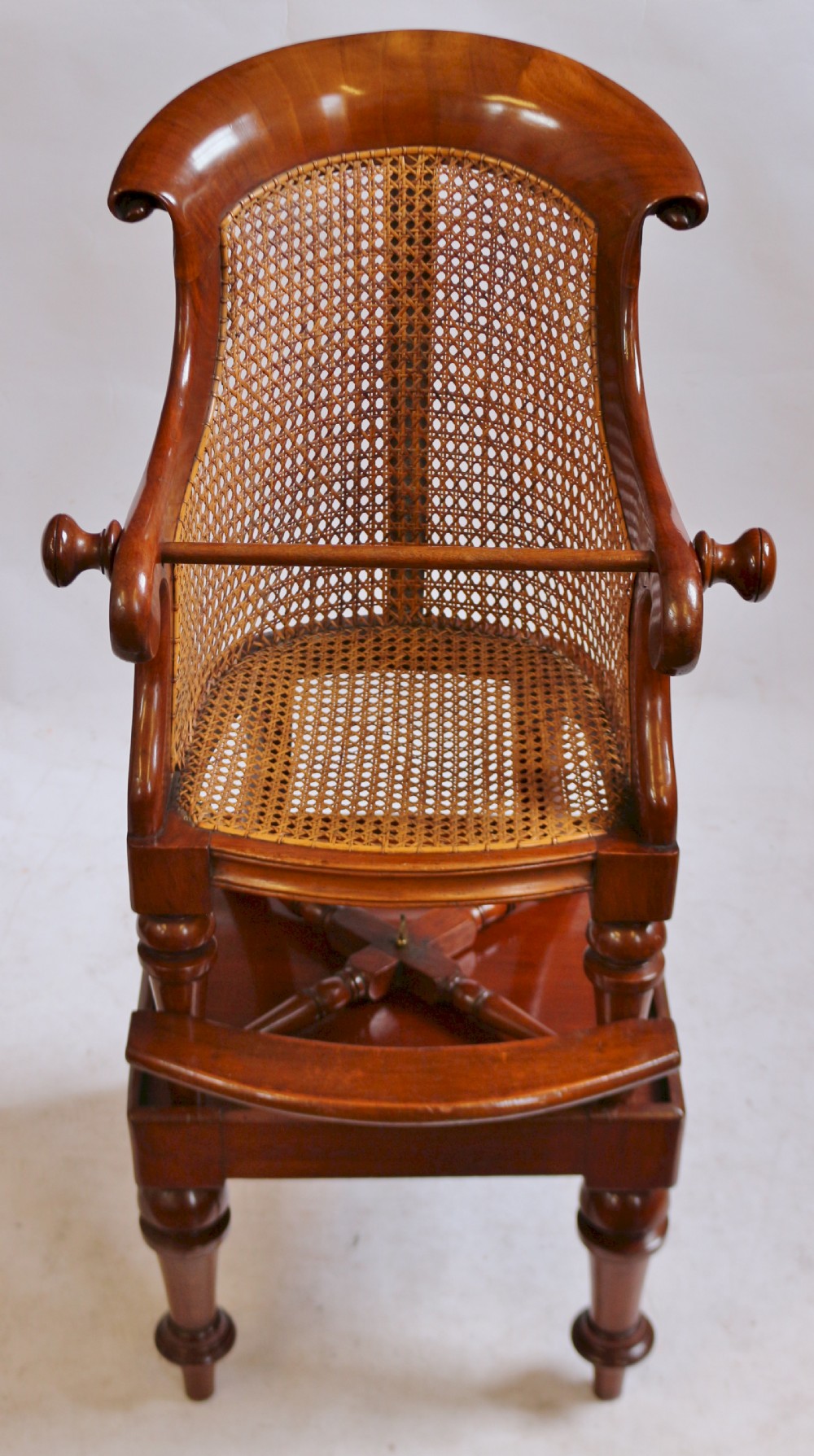 A Victorian mahogany childs high chair featuring a woven cane backrest and seat, turned legs, a protective front bar, and an integrated footrest.