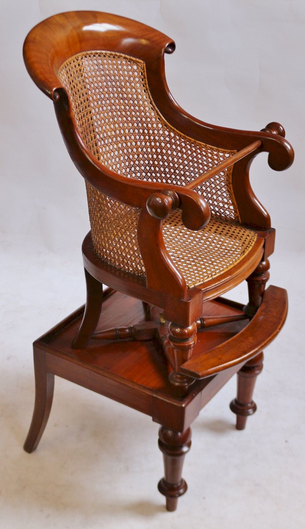 A Victorian mahogany childs high chair featuring a woven cane backrest and seat, turned legs, a protective front bar, and an integrated footrest. View II