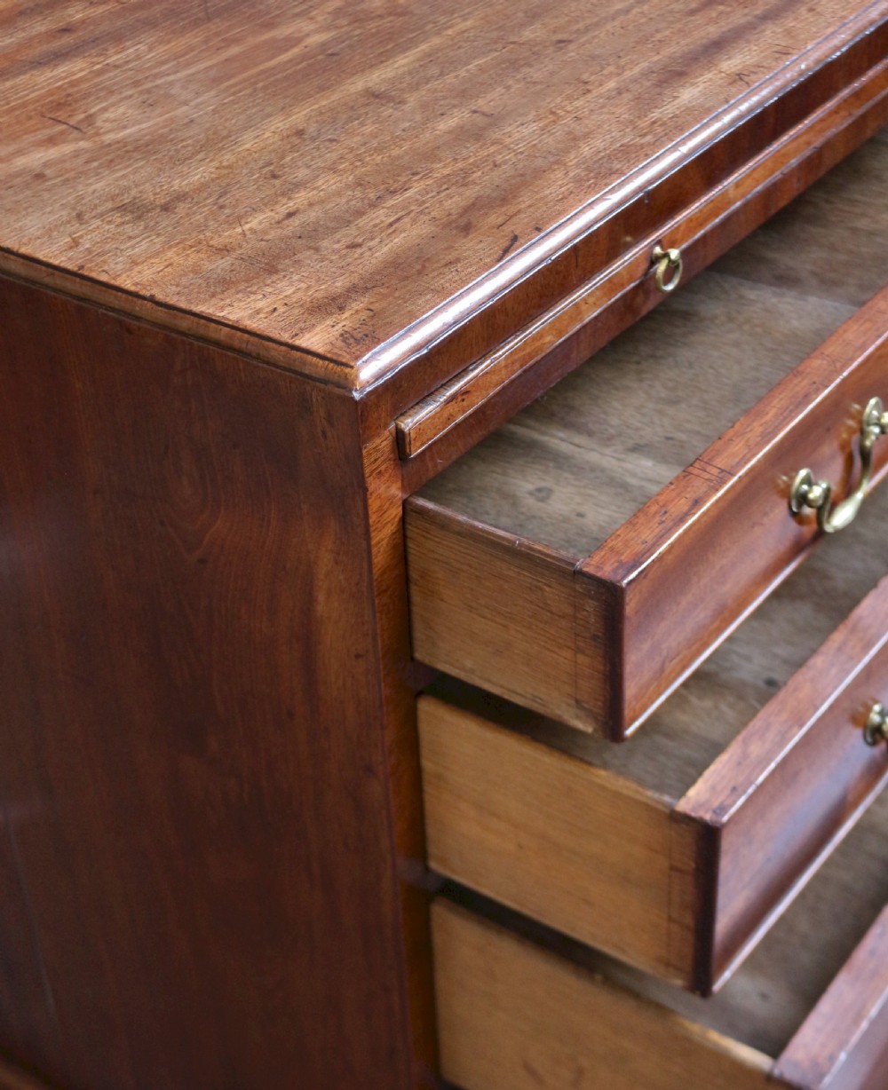 A Georgian mahogany chest of drawers featuring four graduated long drawers with brass swan-neck handles, a pull-out brushing slide, and classic bracket feet. View VII