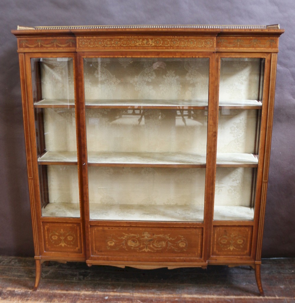 An antique mahogany display cabinet featuring satinwood floral marquetry, a single glazed door, side window panels, and a brass gallery along the top edge.