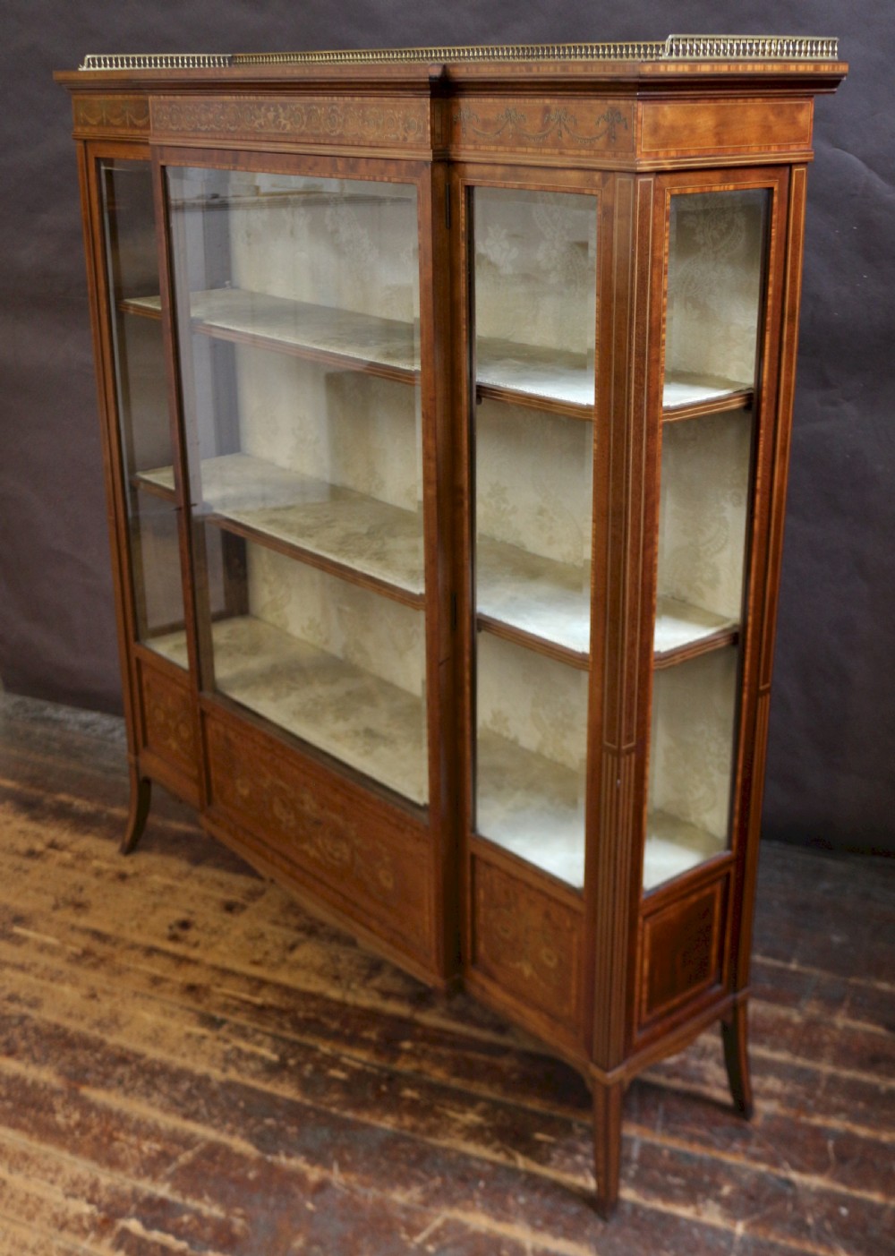 An antique mahogany display cabinet featuring satinwood floral marquetry, a single glazed door, side window panels, and a brass gallery along the top edge. View IV