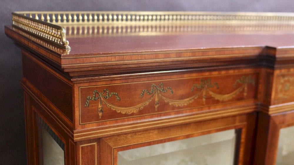 An antique mahogany display cabinet featuring satinwood floral marquetry, a single glazed door, side window panels, and a brass gallery along the top edge. View VI