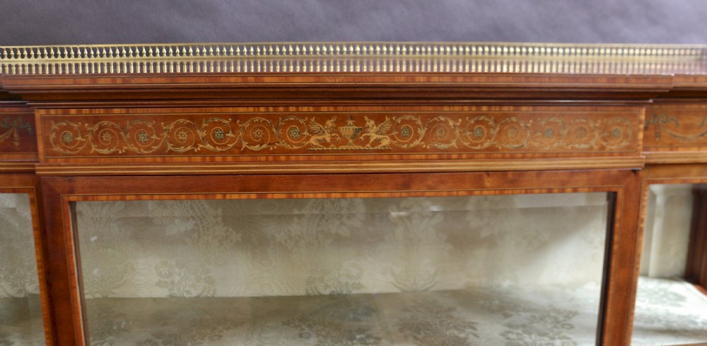 An antique mahogany display cabinet featuring satinwood floral marquetry, a single glazed door, side window panels, and a brass gallery along the top edge. View VII