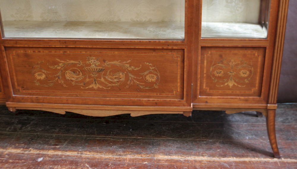 An antique mahogany display cabinet featuring satinwood floral marquetry, a single glazed door, side window panels, and a brass gallery along the top edge. View X