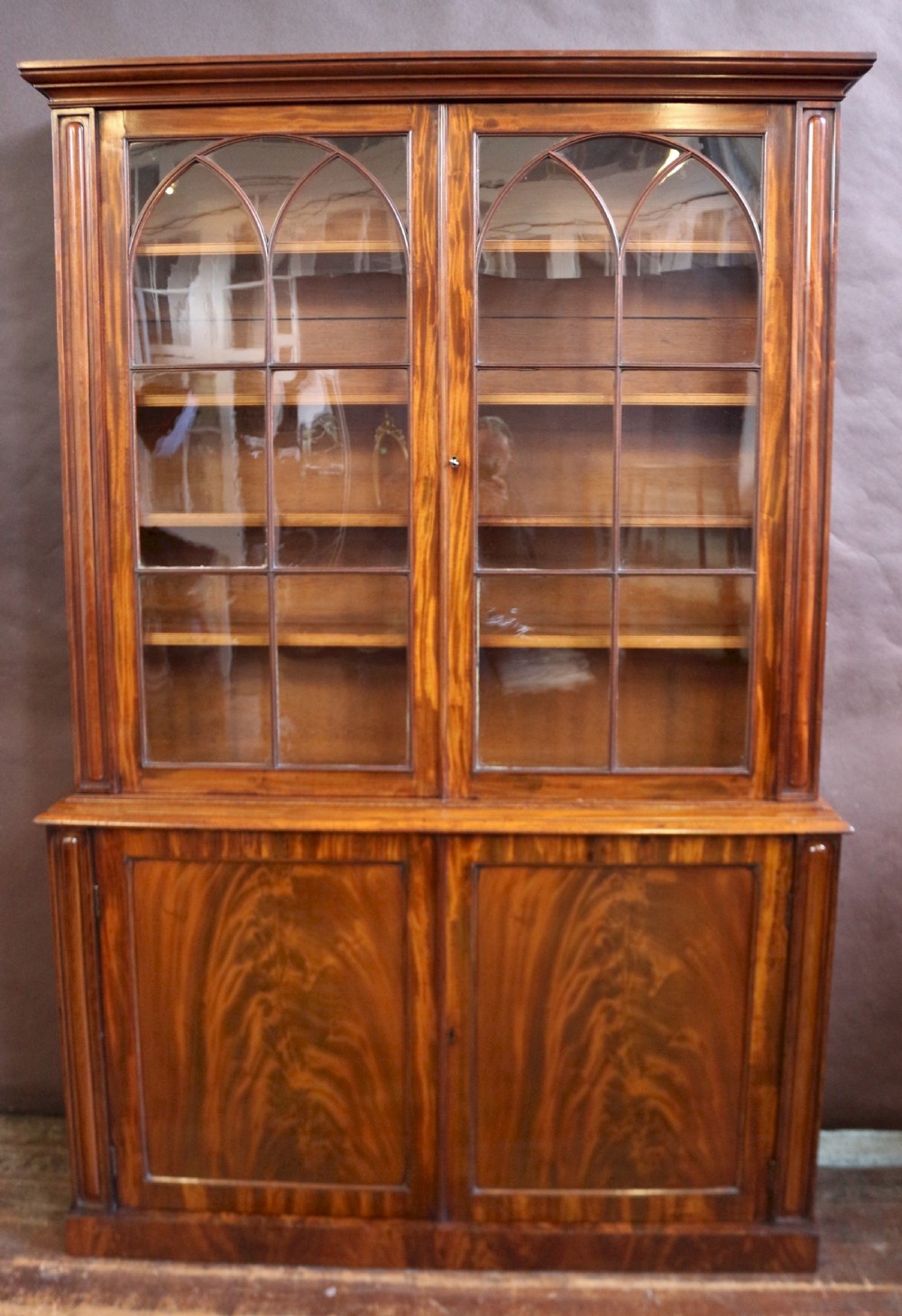 A George IV mahogany bookcase featuring a two-door astragal glazed upper section with gothic arch panes above a two-door cupboard base with flame mahogany grain patterns.