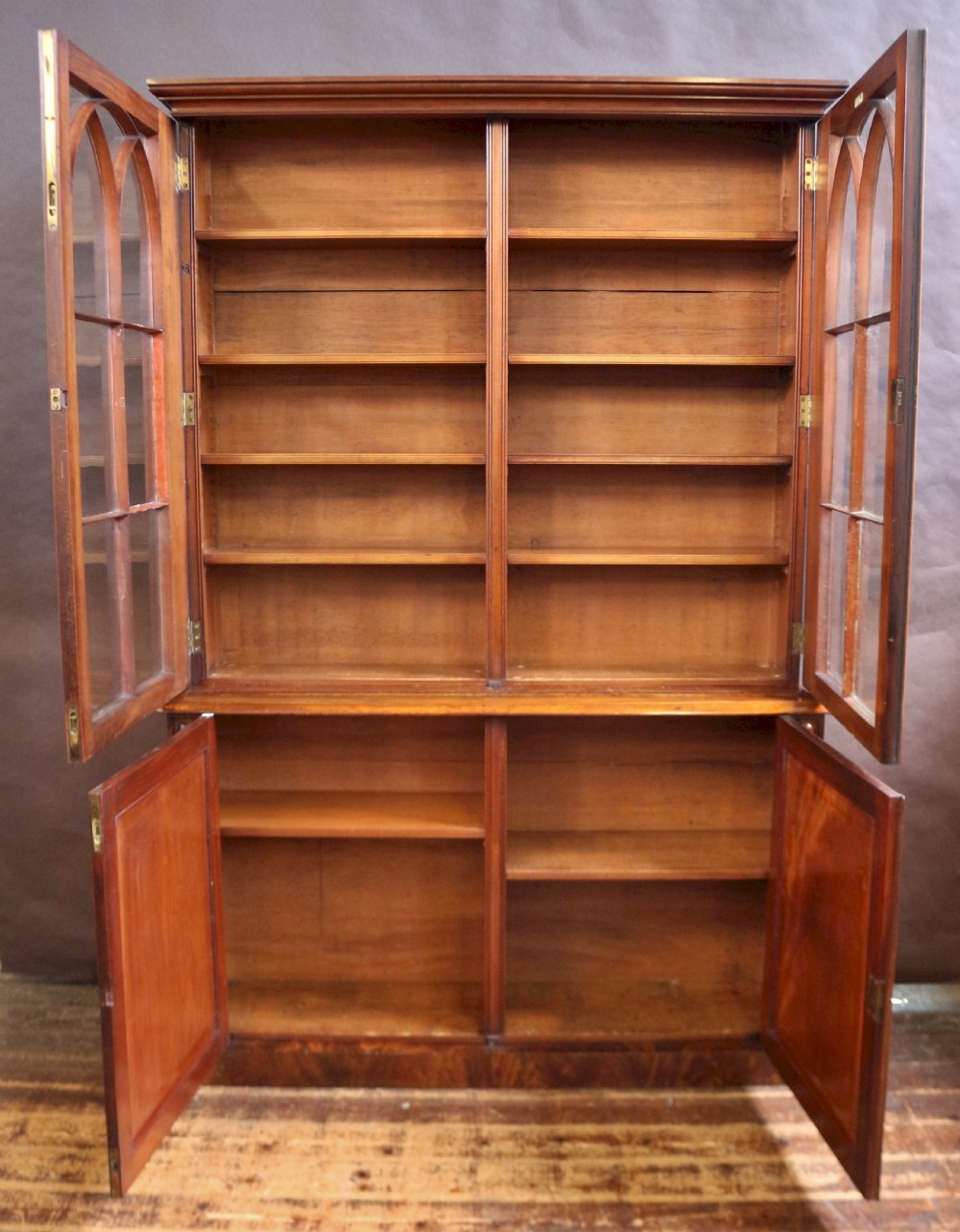 A George IV mahogany bookcase featuring a two-door astragal glazed upper section with gothic arch panes above a two-door cupboard base with flame mahogany grain patterns. View II