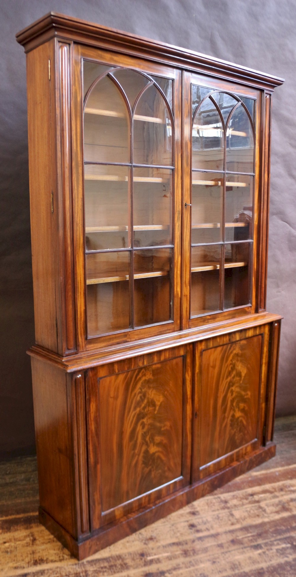 A George IV mahogany bookcase featuring a two-door astragal glazed upper section with gothic arch panes above a two-door cupboard base with flame mahogany grain patterns. View V