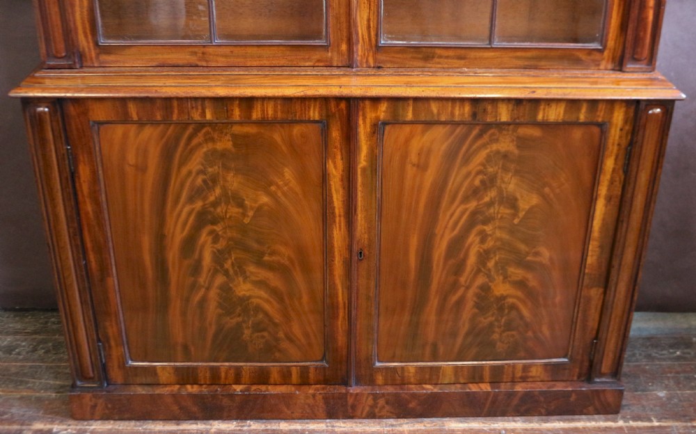 A George IV mahogany bookcase featuring a two-door astragal glazed upper section with gothic arch panes above a two-door cupboard base with flame mahogany grain patterns. View VII