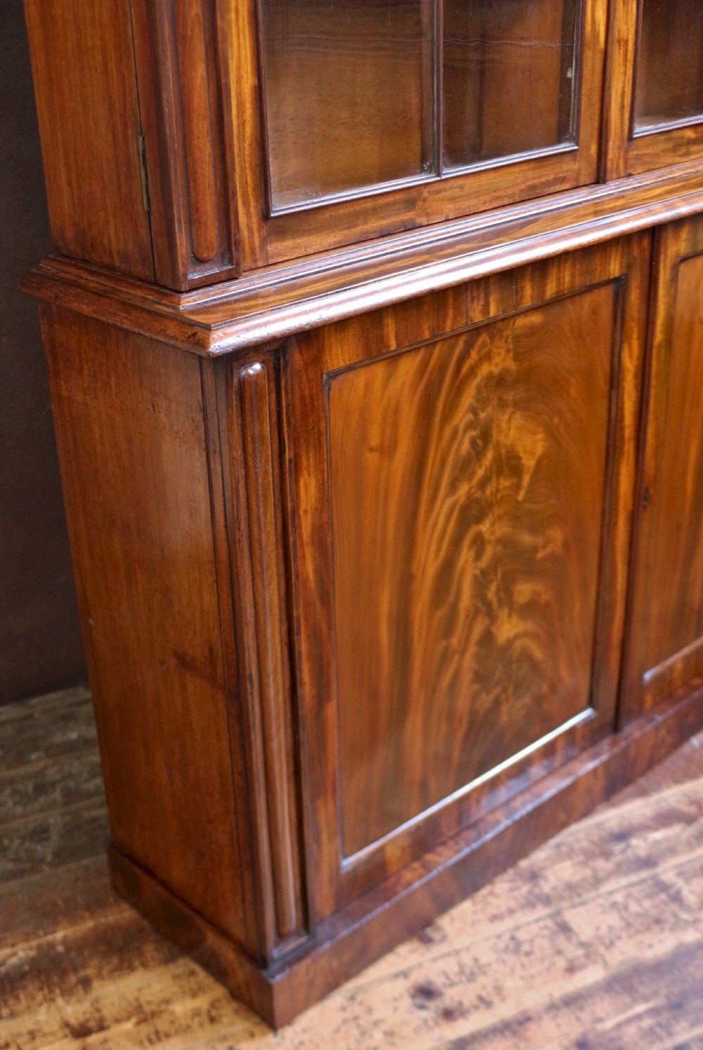 A George IV mahogany bookcase featuring a two-door astragal glazed upper section with gothic arch panes above a two-door cupboard base with flame mahogany grain patterns. View IX