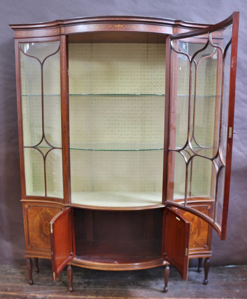A late 19th-century mahogany display cabinet featuring three glazed doors with curved astragal glazing bars above inlaid lower panels and turned legs. View II