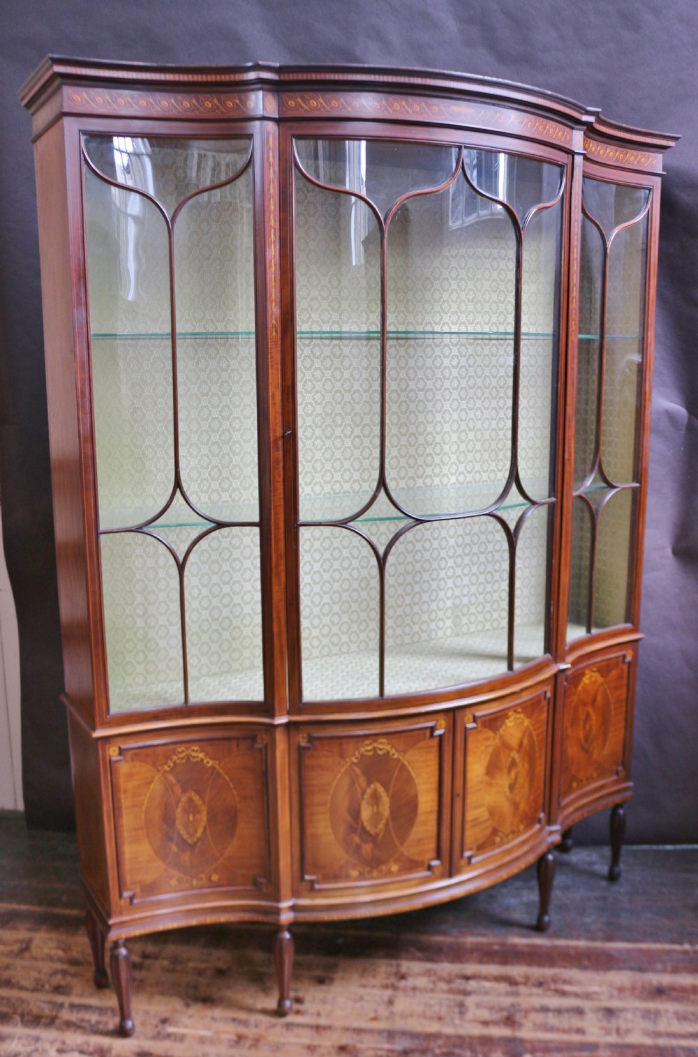 A late 19th-century mahogany display cabinet featuring three glazed doors with curved astragal glazing bars above inlaid lower panels and turned legs. View III