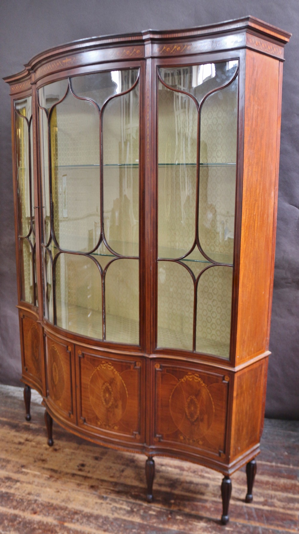 A late 19th-century mahogany display cabinet featuring three glazed doors with curved astragal glazing bars above inlaid lower panels and turned legs. View V