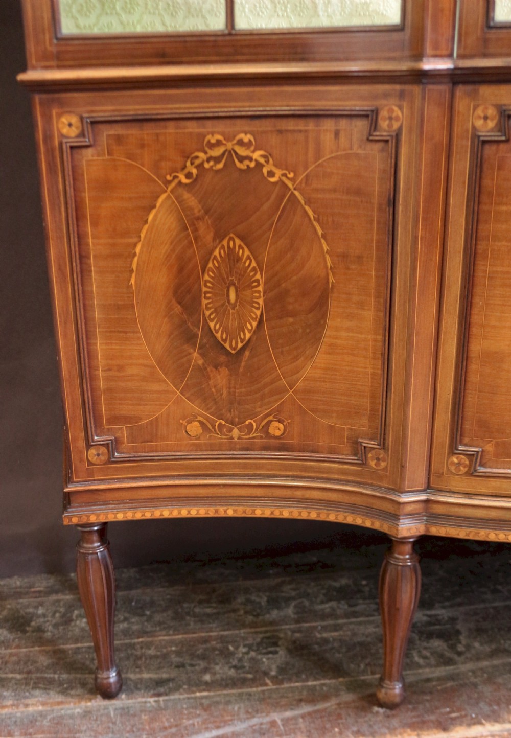 A late 19th-century mahogany display cabinet featuring three glazed doors with curved astragal glazing bars above inlaid lower panels and turned legs. View VII