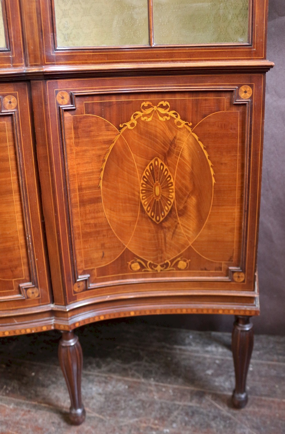 A late 19th-century mahogany display cabinet featuring three glazed doors with curved astragal glazing bars above inlaid lower panels and turned legs. View IX