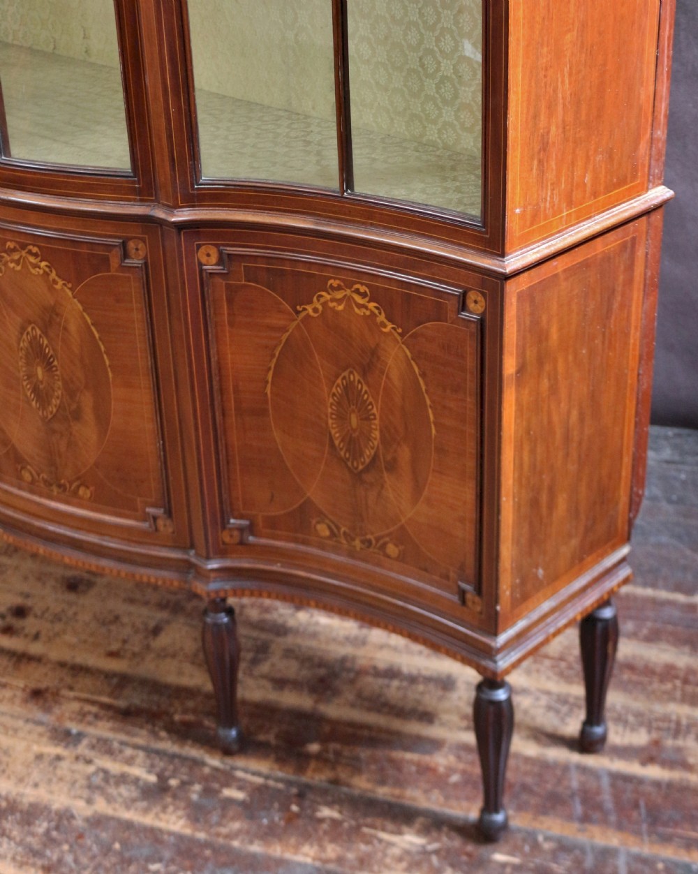 A late 19th-century mahogany display cabinet featuring three glazed doors with curved astragal glazing bars above inlaid lower panels and turned legs. View X