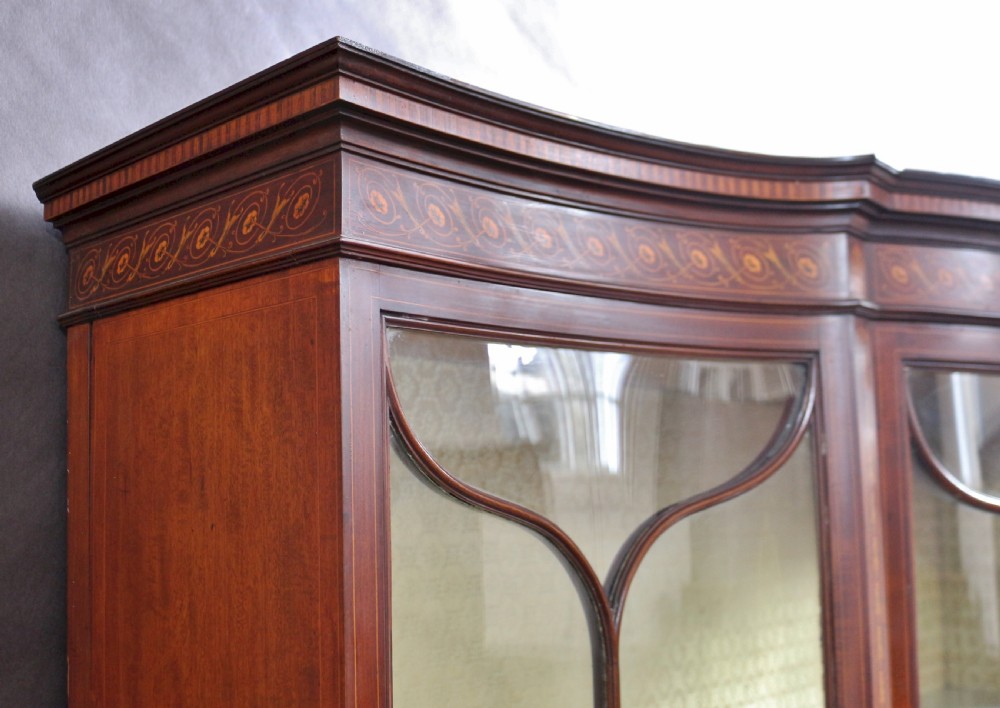 A late 19th-century mahogany display cabinet featuring three glazed doors with curved astragal glazing bars above inlaid lower panels and turned legs. View XI