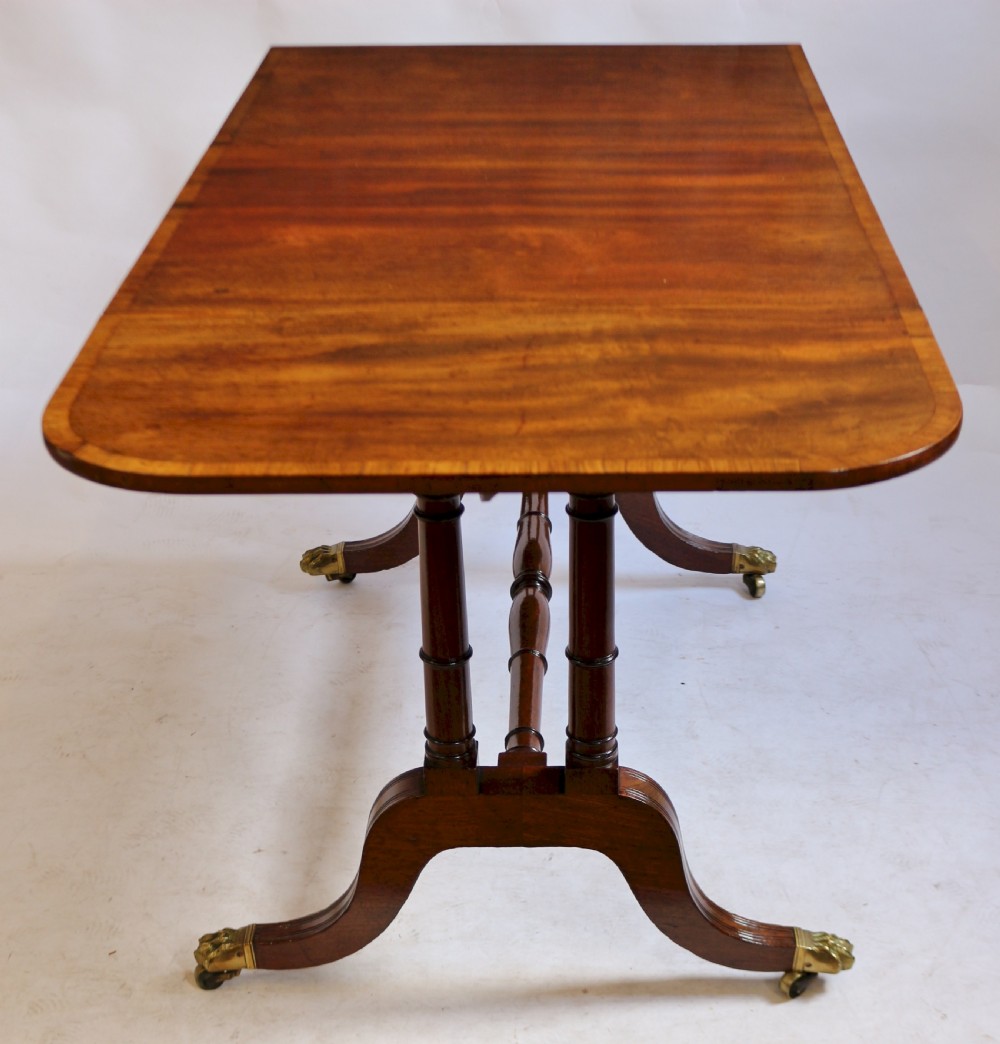 A Regency mahogany sofa table featuring drop-leaf ends, satinwood crossbanding, two frieze drawers, and splayed legs terminating in brass paw castors. View VI