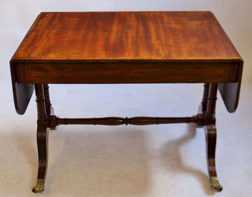 A Regency mahogany sofa table featuring drop-leaf ends, satinwood crossbanding, two frieze drawers, and splayed legs terminating in brass paw castors. View VII