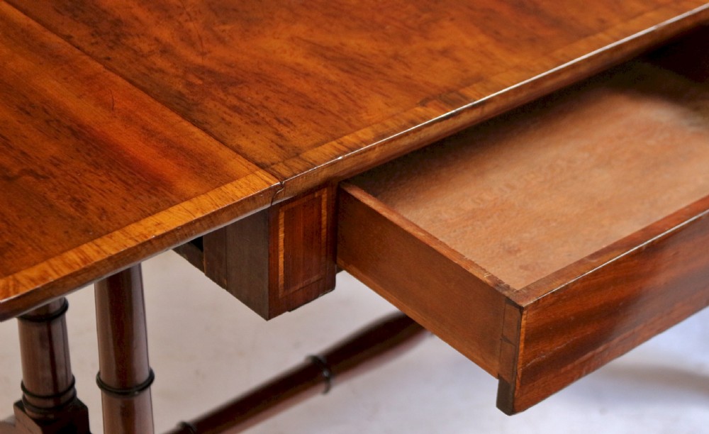 A Regency mahogany sofa table featuring drop-leaf ends, satinwood crossbanding, two frieze drawers, and splayed legs terminating in brass paw castors. View VIII