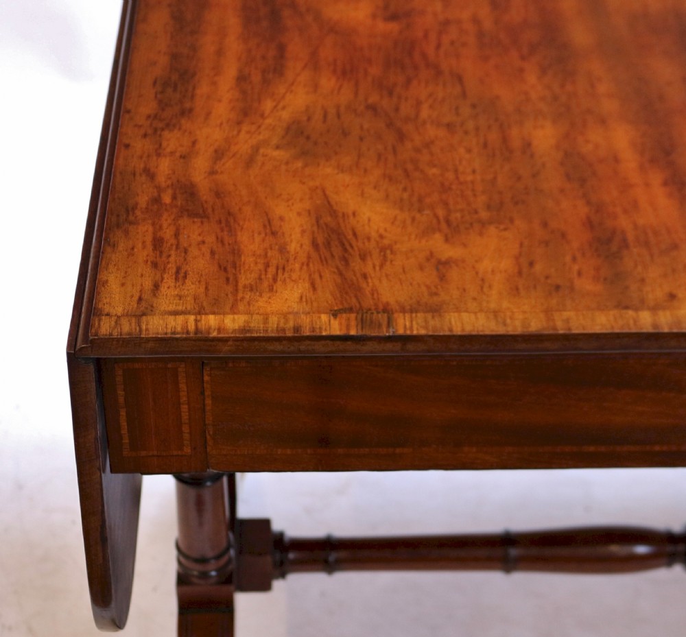 A Regency mahogany sofa table featuring drop-leaf ends, satinwood crossbanding, two frieze drawers, and splayed legs terminating in brass paw castors. View IX