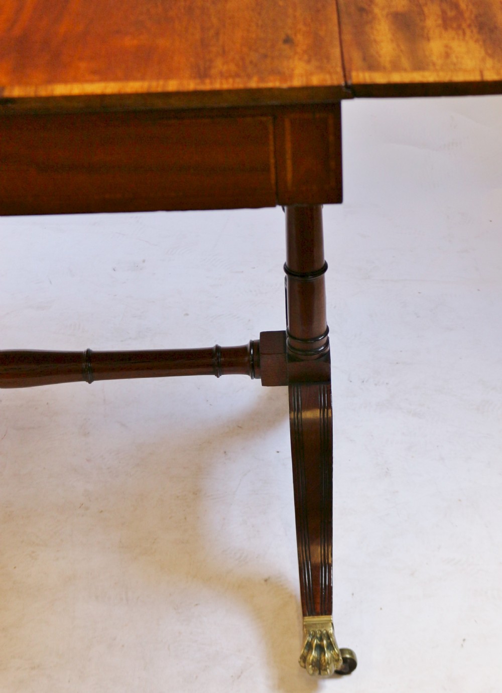 A Regency mahogany sofa table featuring drop-leaf ends, satinwood crossbanding, two frieze drawers, and splayed legs terminating in brass paw castors. View X