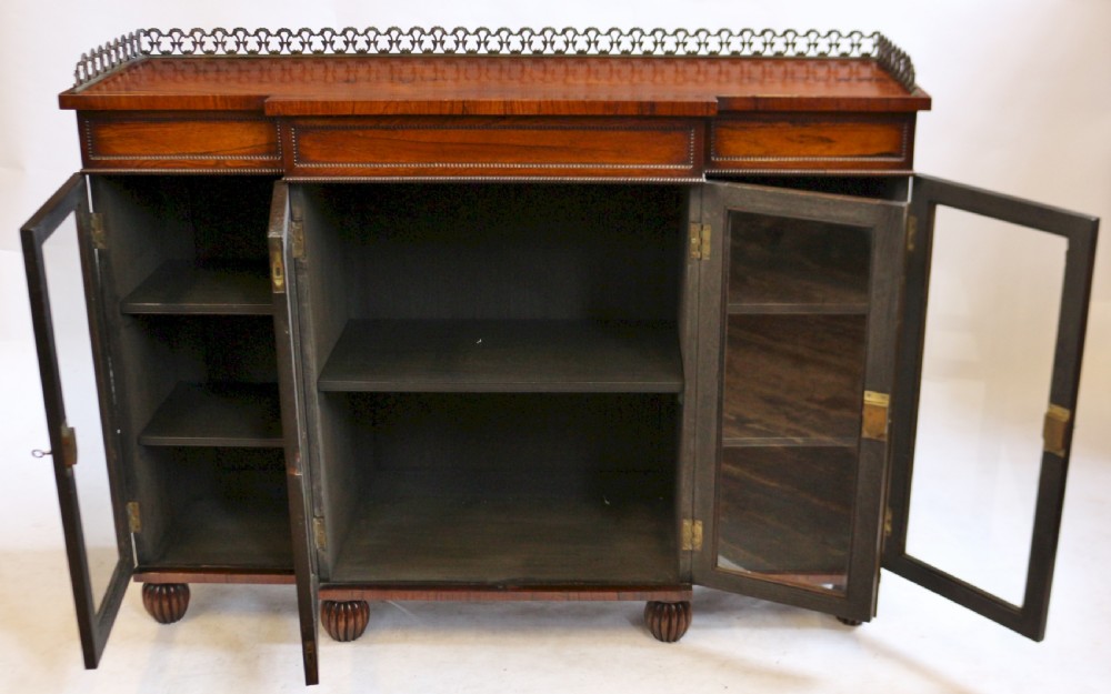 An antique Regency rosewood breakfront side cabinet featuring four glazed doors, a brass gallery rail along the top, and turned fluted feet. View II
