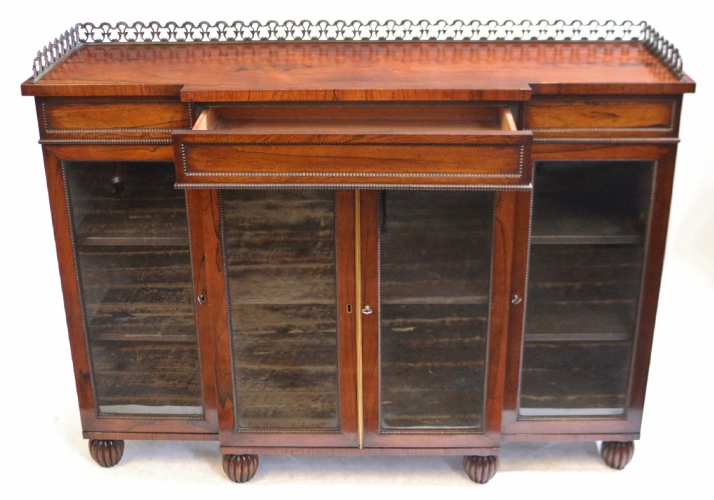 An antique Regency rosewood breakfront side cabinet featuring four glazed doors, a brass gallery rail along the top, and turned fluted feet. View III