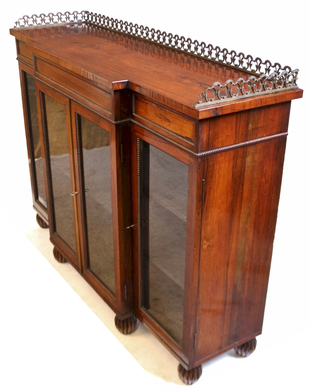 An antique Regency rosewood breakfront side cabinet featuring four glazed doors, a brass gallery rail along the top, and turned fluted feet. View VI