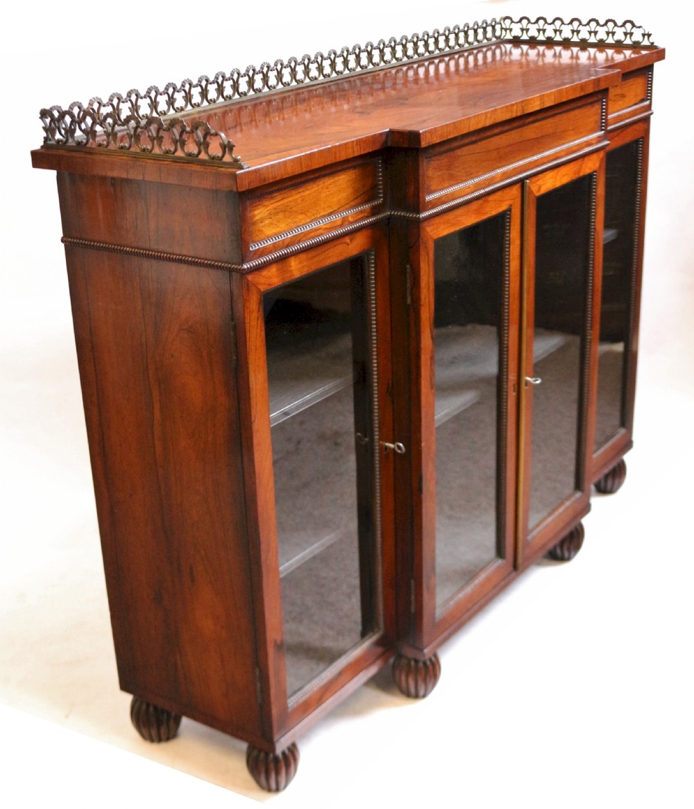 An antique Regency rosewood breakfront side cabinet featuring four glazed doors, a brass gallery rail along the top, and turned fluted feet. View VII