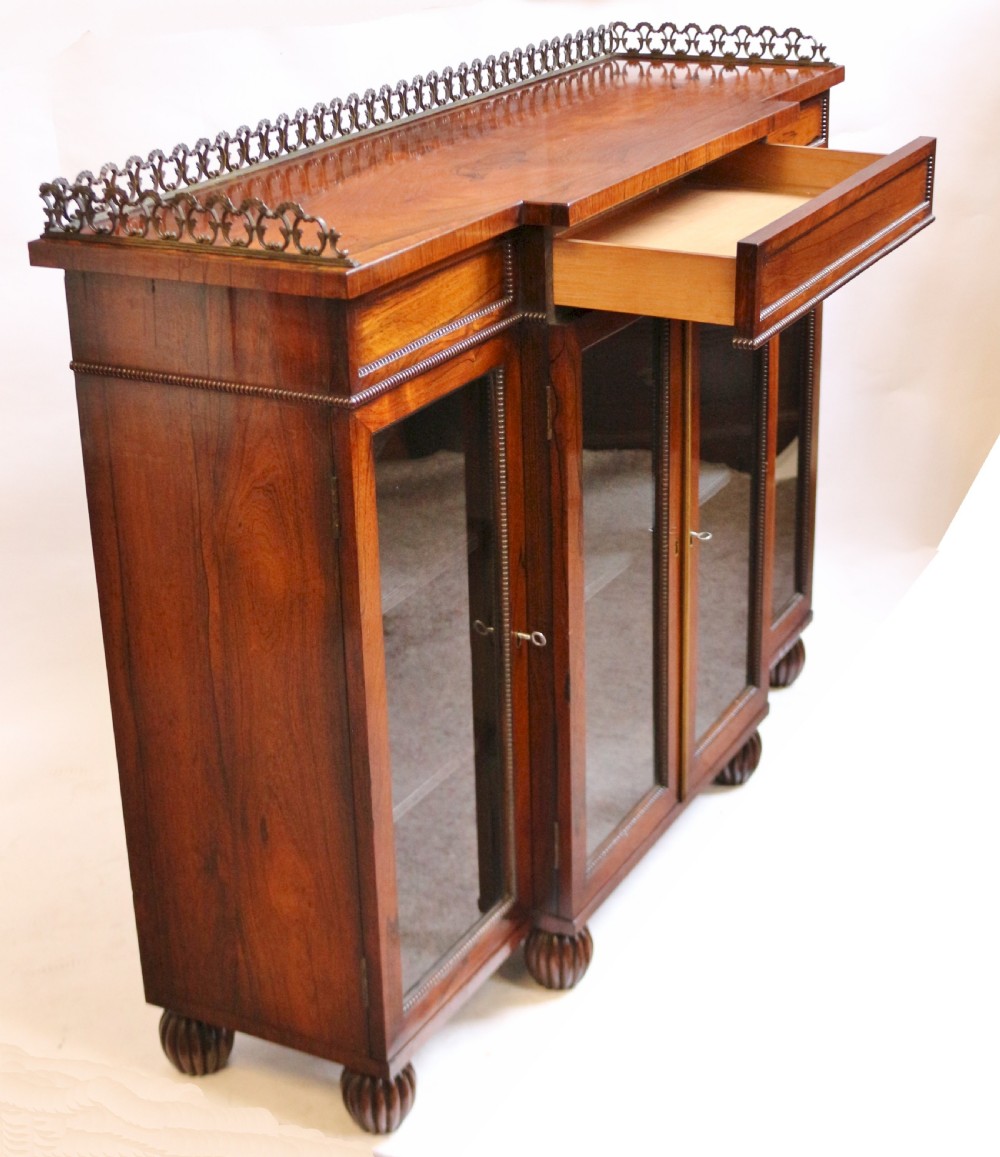 An antique Regency rosewood breakfront side cabinet featuring four glazed doors, a brass gallery rail along the top, and turned fluted feet. View VIII