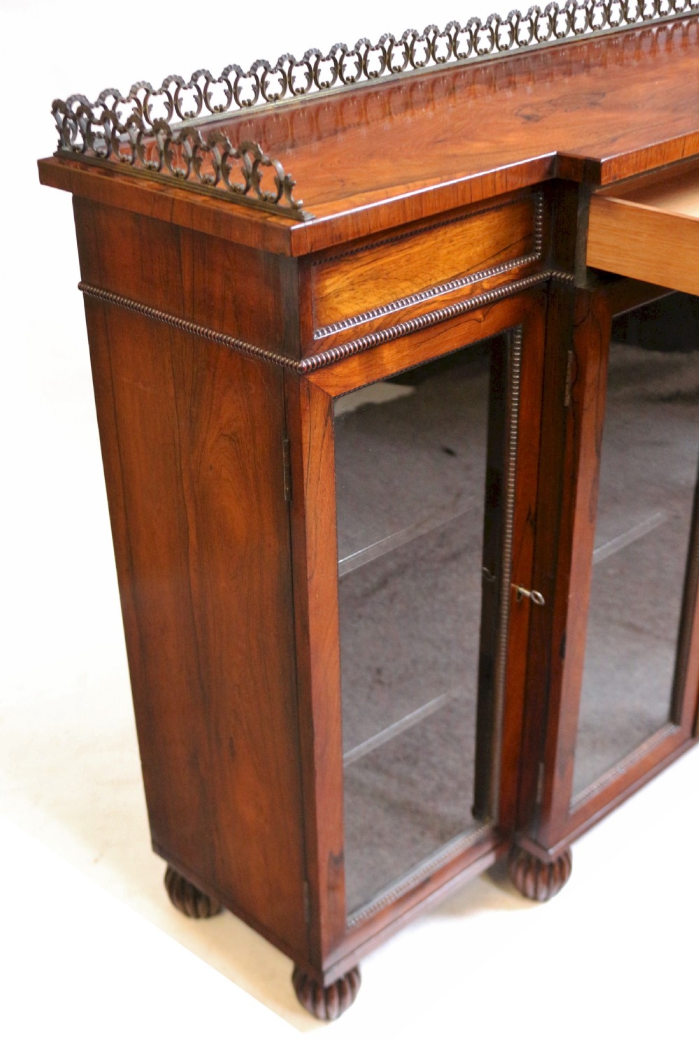 An antique Regency rosewood breakfront side cabinet featuring four glazed doors, a brass gallery rail along the top, and turned fluted feet. View X