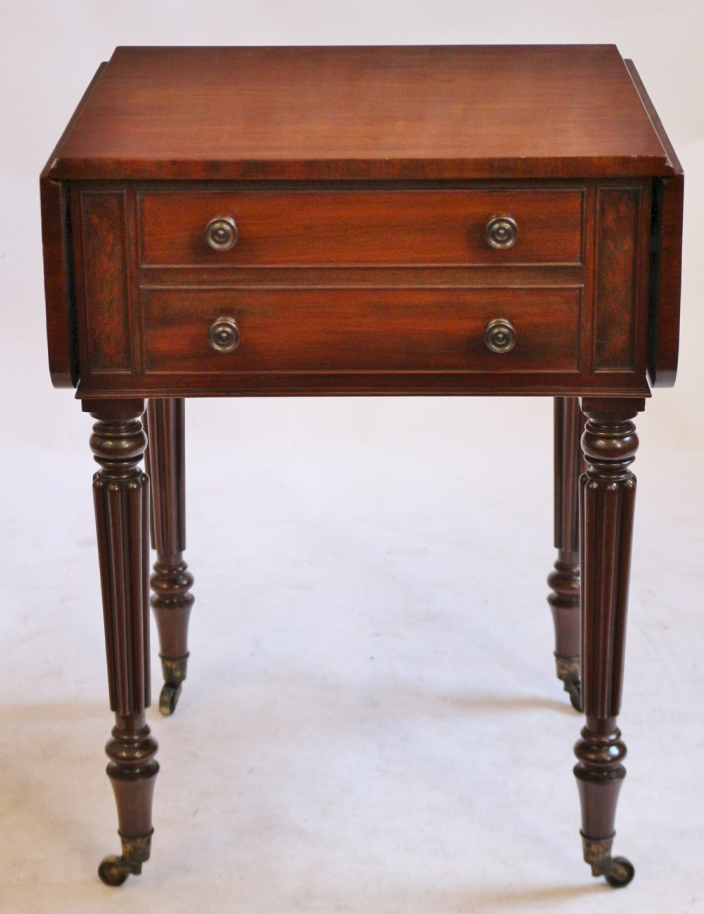 A William IV mahogany drop-leaf side table featuring two drawers with turned knobs, brass keyhole escutcheons, and reeded legs on brass castors. View VI