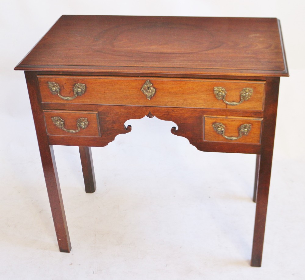 A George III mahogany lowboy featuring three drawers with brass handles, a central shaped apron, and four square legs.