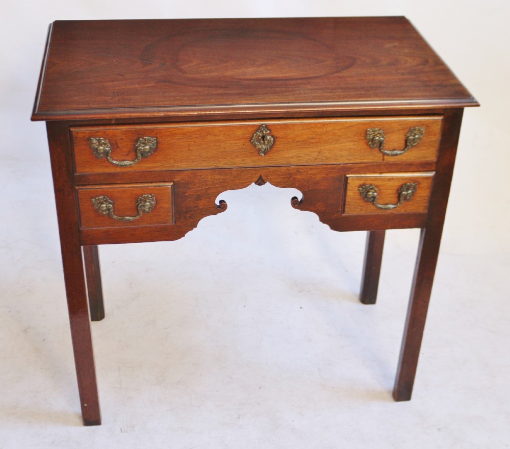 A George III mahogany lowboy featuring three drawers with brass handles, a central shaped apron, and four square legs. View II