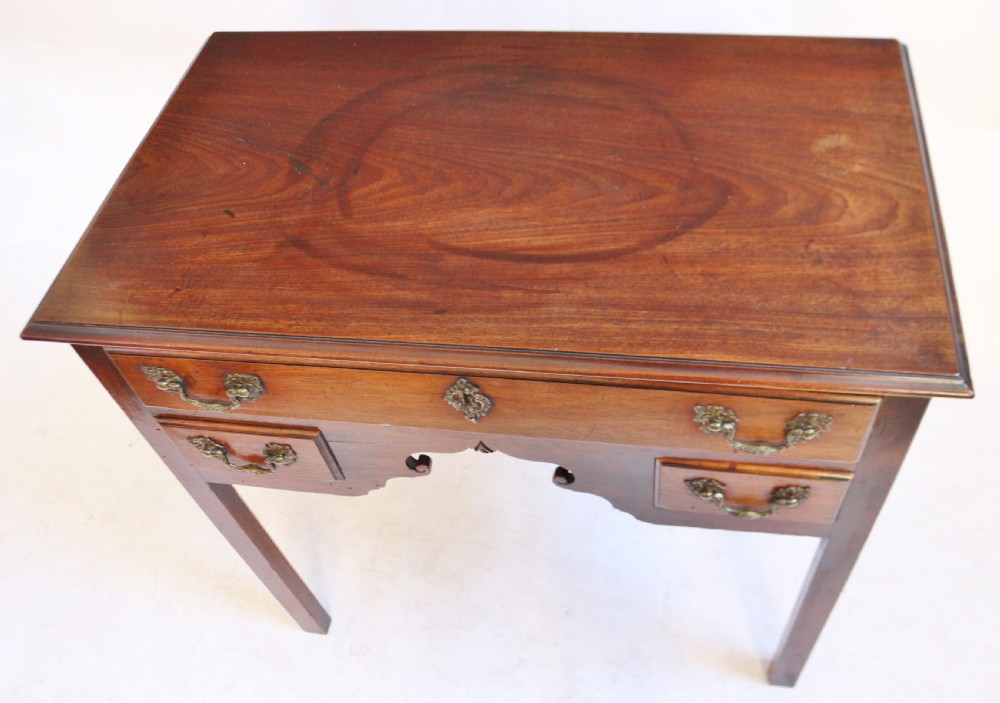 A George III mahogany lowboy featuring three drawers with brass handles, a central shaped apron, and four square legs. View III