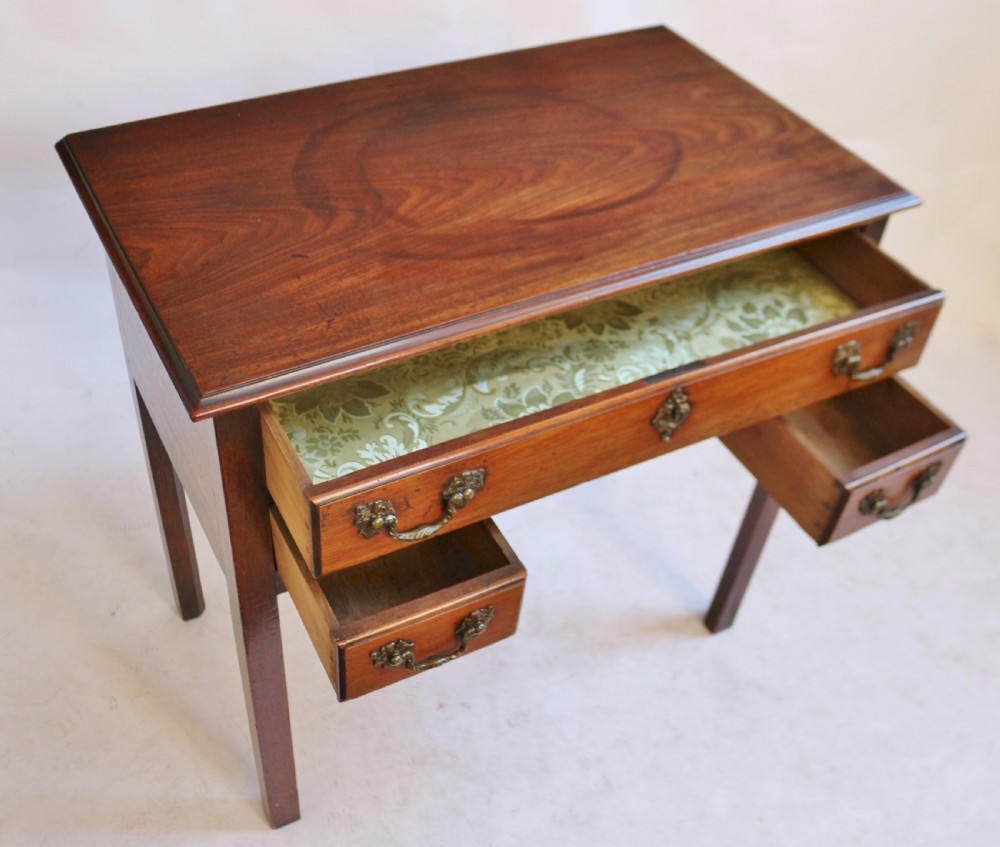 A George III mahogany lowboy featuring three drawers with brass handles, a central shaped apron, and four square legs. View IV