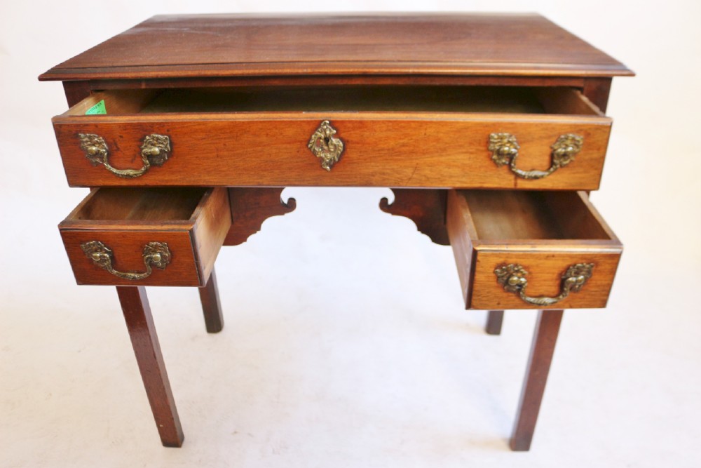A George III mahogany lowboy featuring three drawers with brass handles, a central shaped apron, and four square legs. View V