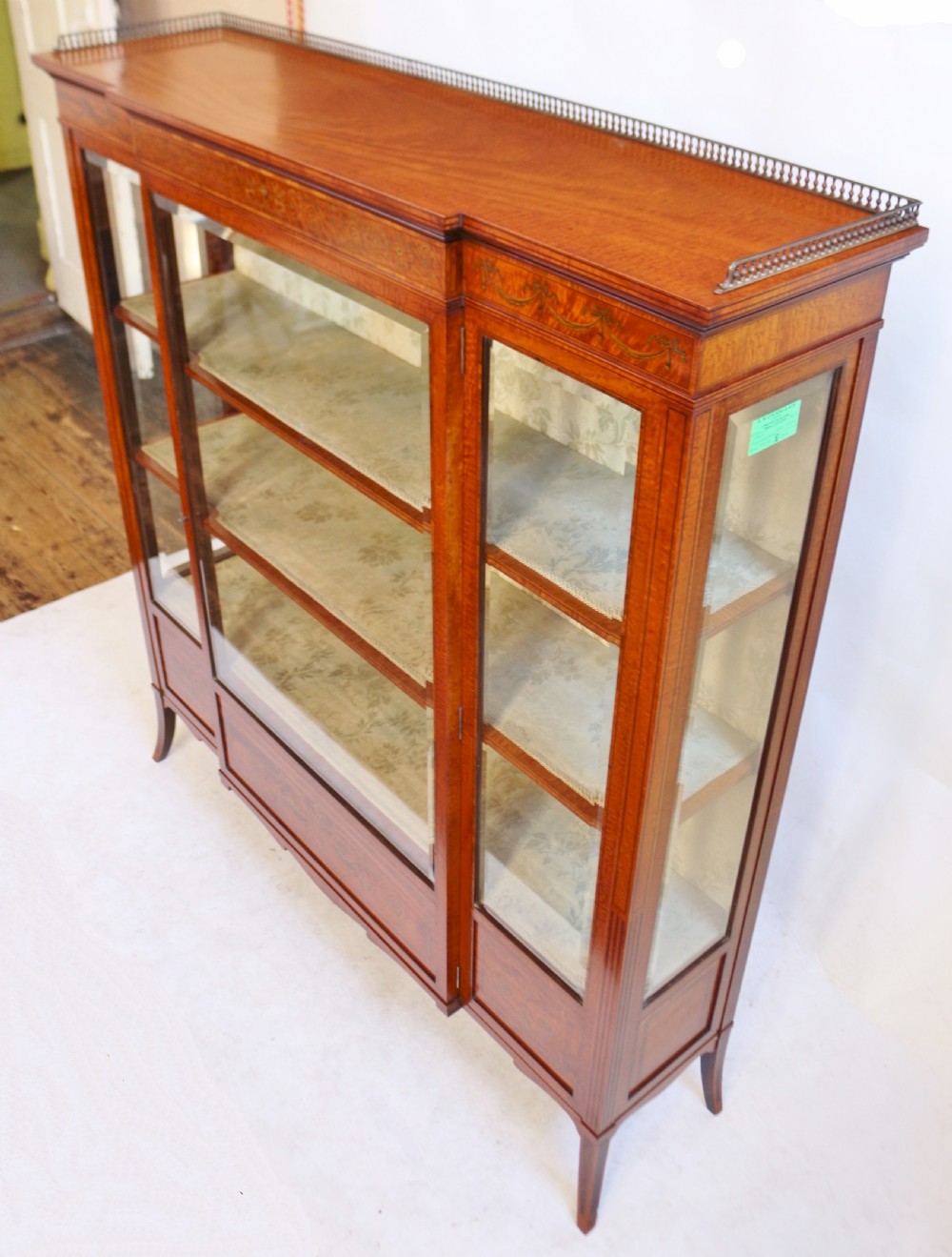 An antique satinwood display cabinet featuring a single central glazed door, fabric-lined interior shelves, floral marquetry inlay, and slightly splayed legs. View III