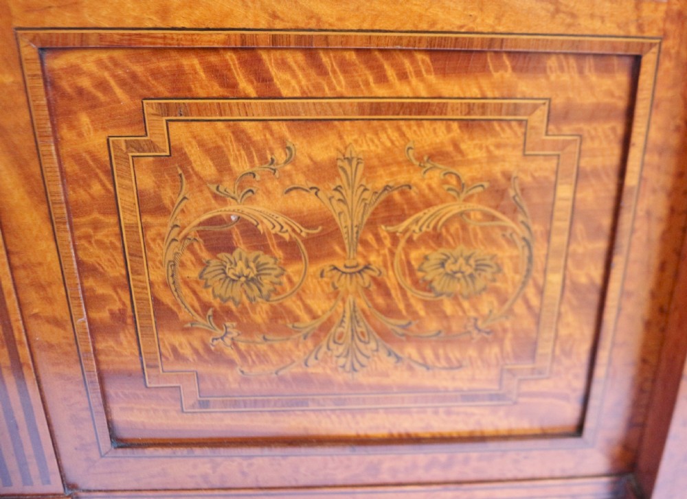 An antique satinwood display cabinet featuring a single central glazed door, fabric-lined interior shelves, floral marquetry inlay, and slightly splayed legs. View V
