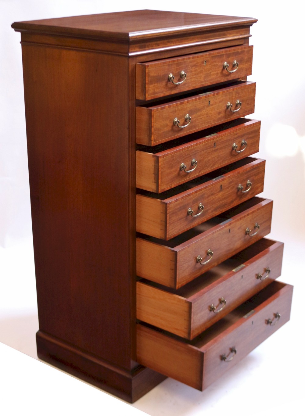 An Edwardian mahogany Wellington chest featuring seven stacked drawers with decorative wood inlay, brass drop handles, and a plinth base. View III