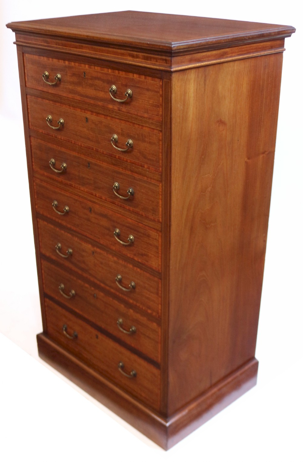 An Edwardian mahogany Wellington chest featuring seven stacked drawers with decorative wood inlay, brass drop handles, and a plinth base. View IV