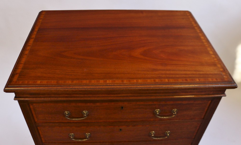An Edwardian mahogany Wellington chest featuring seven stacked drawers with decorative wood inlay, brass drop handles, and a plinth base. View V