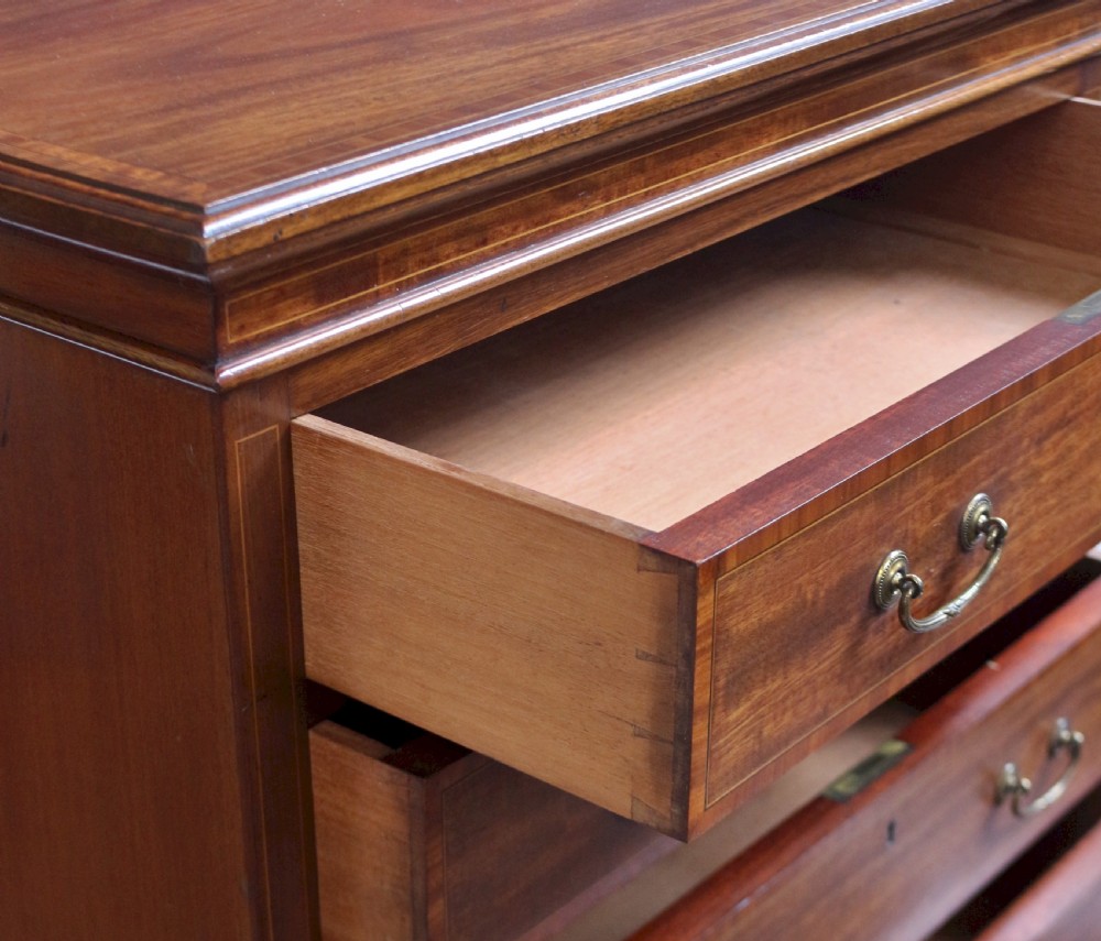 An Edwardian mahogany Wellington chest featuring seven stacked drawers with decorative wood inlay, brass drop handles, and a plinth base. View VII