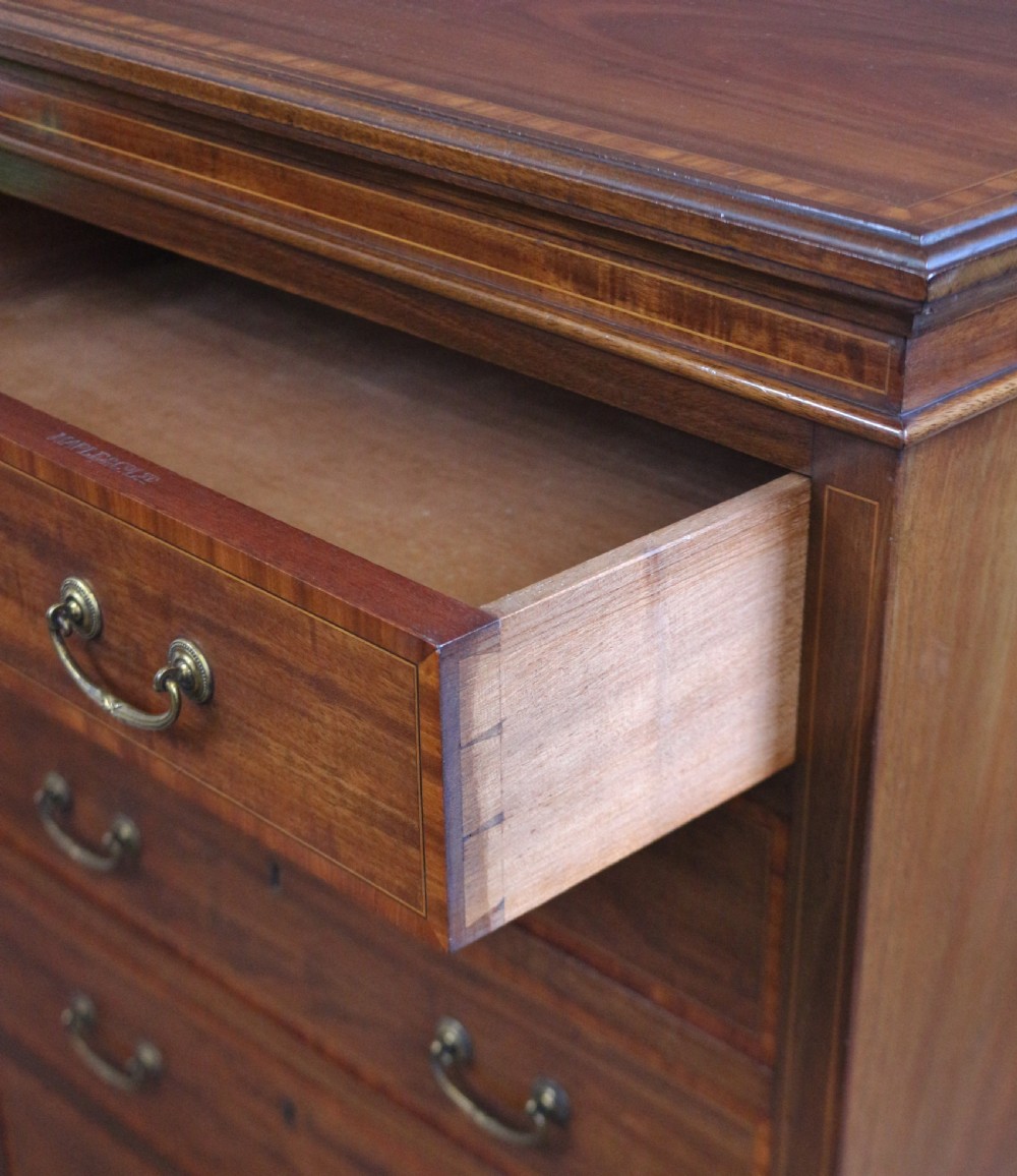 An Edwardian mahogany Wellington chest featuring seven stacked drawers with decorative wood inlay, brass drop handles, and a plinth base. View VIII