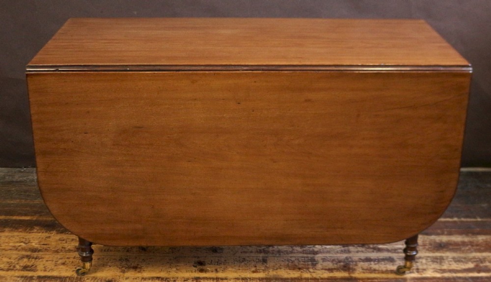 A George IV mahogany drop-leaf dining table shown with both side flaps folded down, featuring turned wooden legs and brass castors.