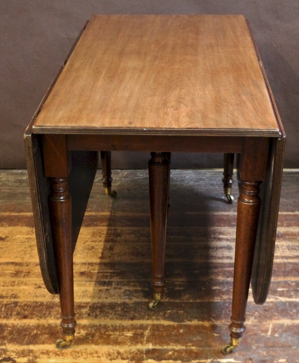 A George IV mahogany drop-leaf dining table shown with both side flaps folded down, featuring turned wooden legs and brass castors. View II
