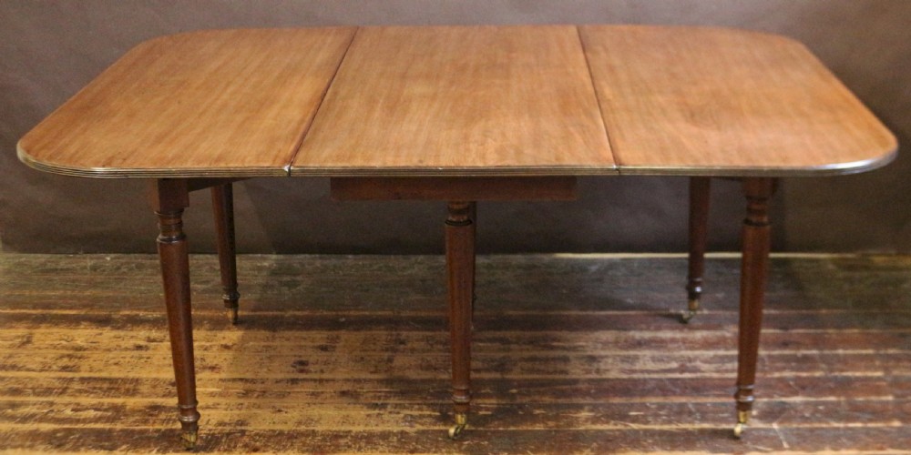 A George IV mahogany drop-leaf dining table shown with both side flaps folded down, featuring turned wooden legs and brass castors. View III
